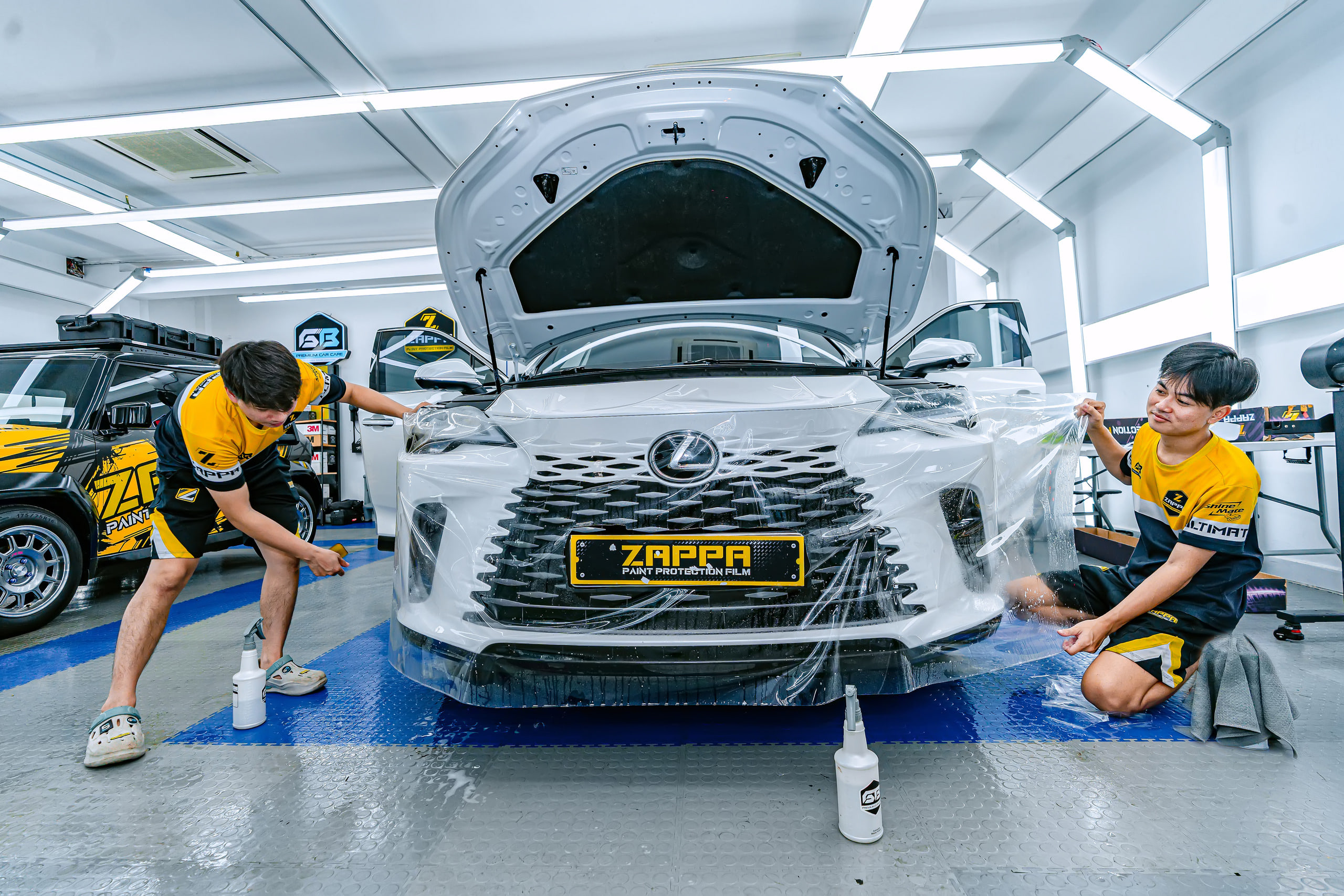 Hai kỹ thuật viên dán PPF cản trước Lexus RX trong phòng kín ở Store Detailing Bình Tân